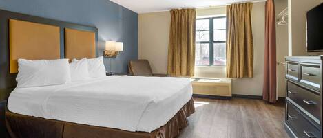 A hotel room with a large bed, a desk, a chair, a TV, and a dresser.