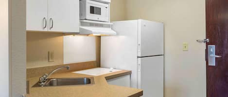 A compact kitchen with white cabinets, a microwave, a refrigerator, a sink, and a countertop.