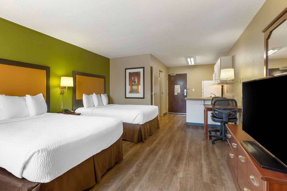 A hotel room with two beds, a desk with a chair, a television, and a door leading to a bathroom.
