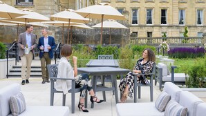 Un'area patio esterna con tavoli e sedie, ombrelloni e un edificio sullo sfondo.