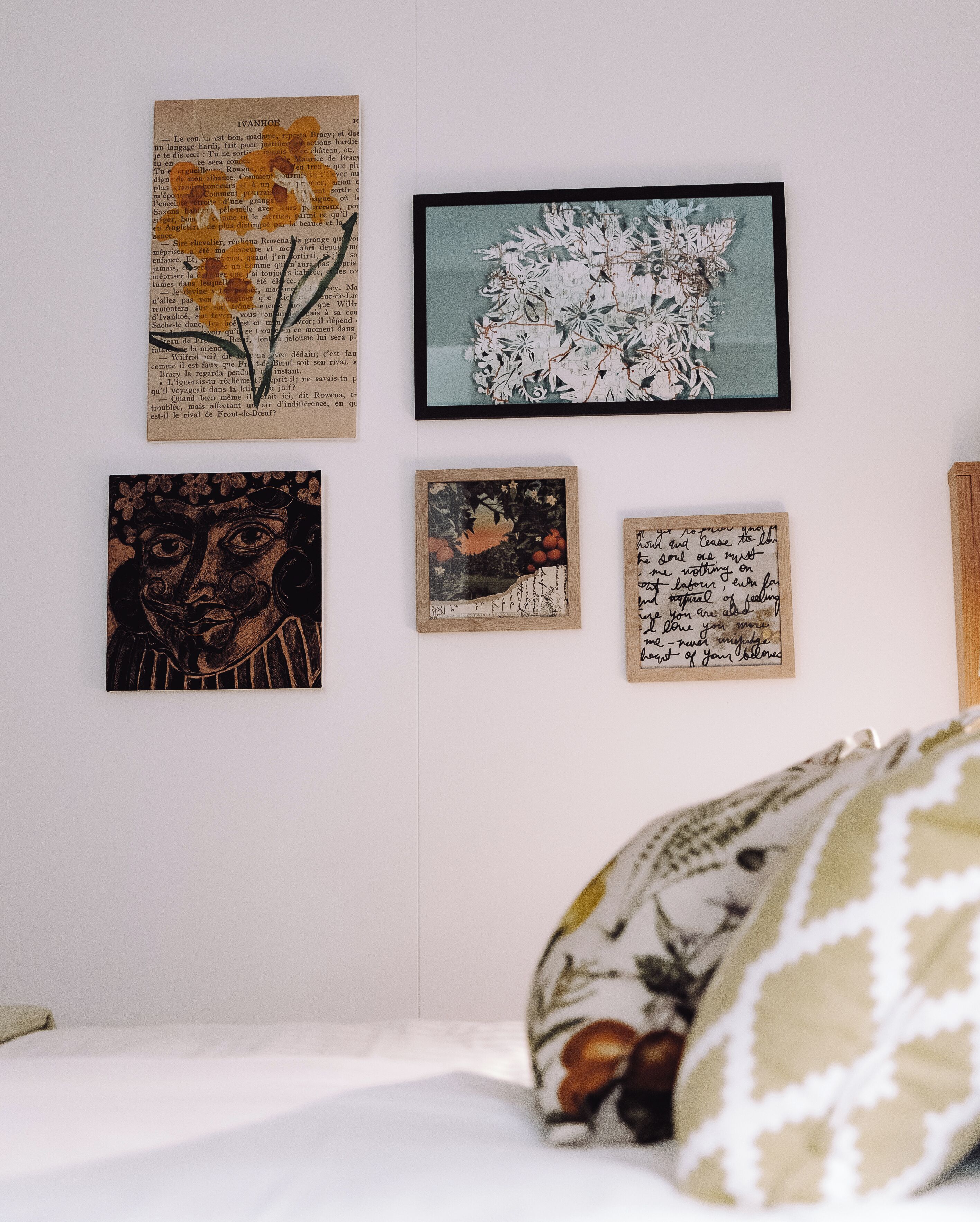 A bedroom with a bed, a pillow, and four framed artworks on the wall.