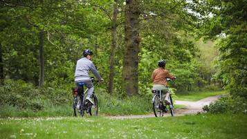 Dos ciclistas en un sendero estrecho bordeado de árboles en un área verde y exuberante.
