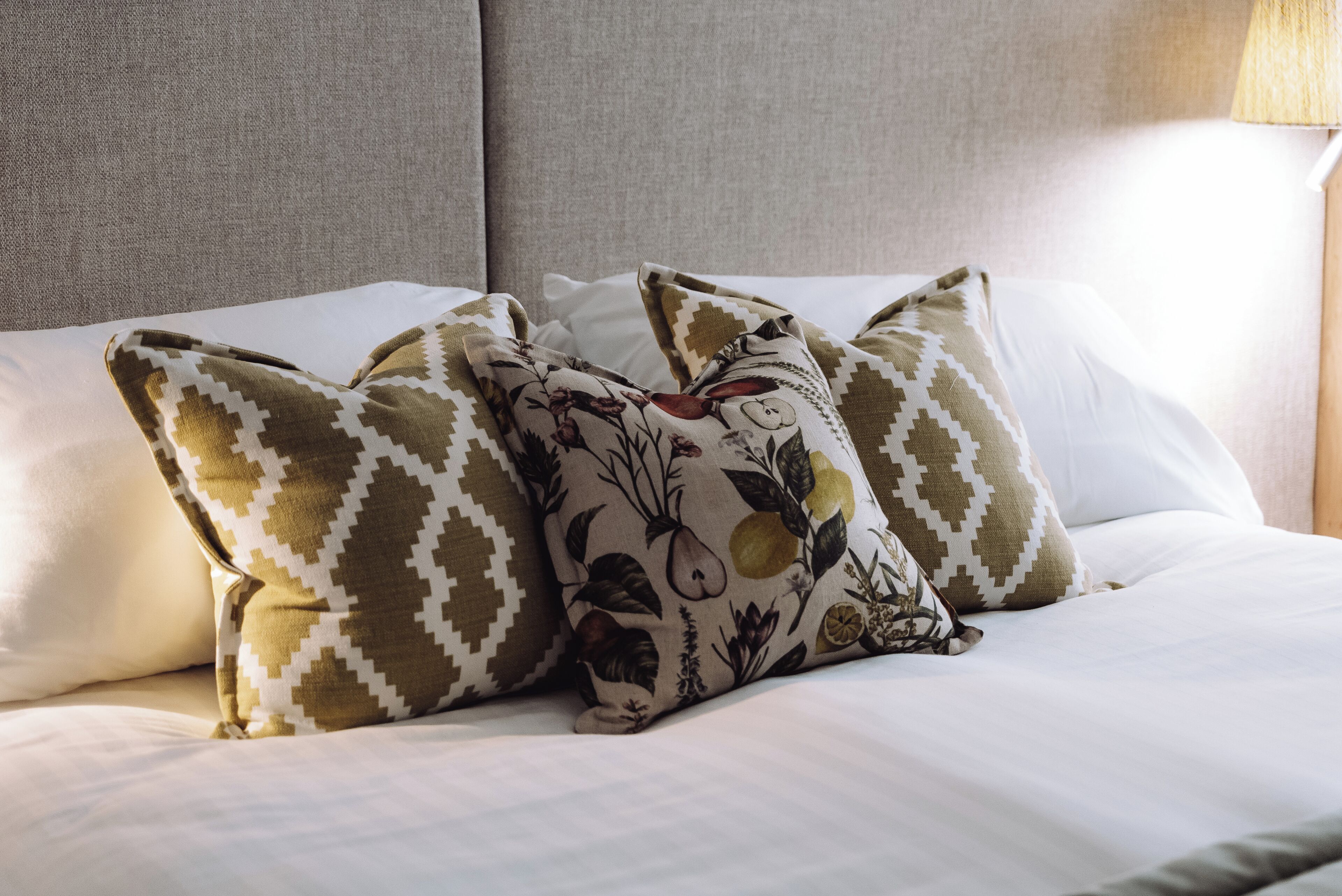 Una cama con ropa de cama blanca y almohadas decorativas con motivos geométricos y florales.