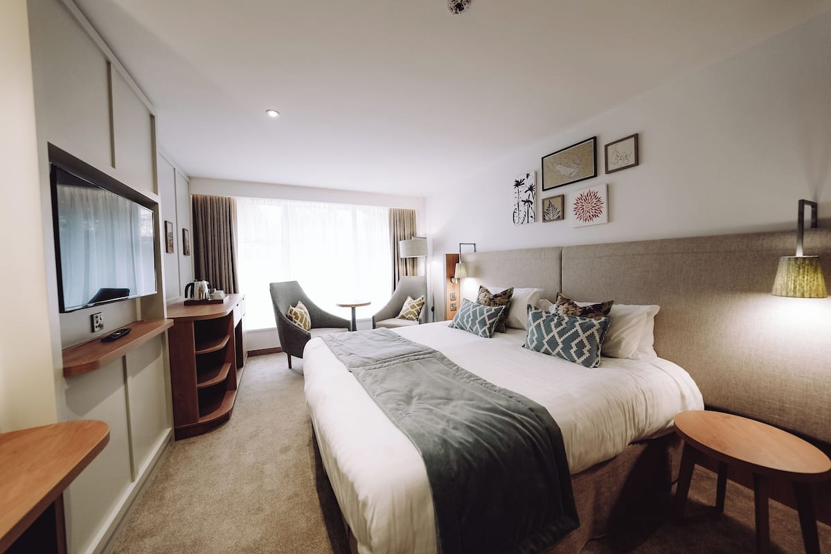 Camera d'albergo con un letto grande, una scrivania, una sedia, una televisione e una finestra con tende.