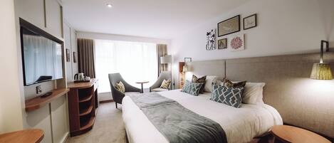 A hotel room with a large bed, a desk, a chair, a TV, and a window with curtains.