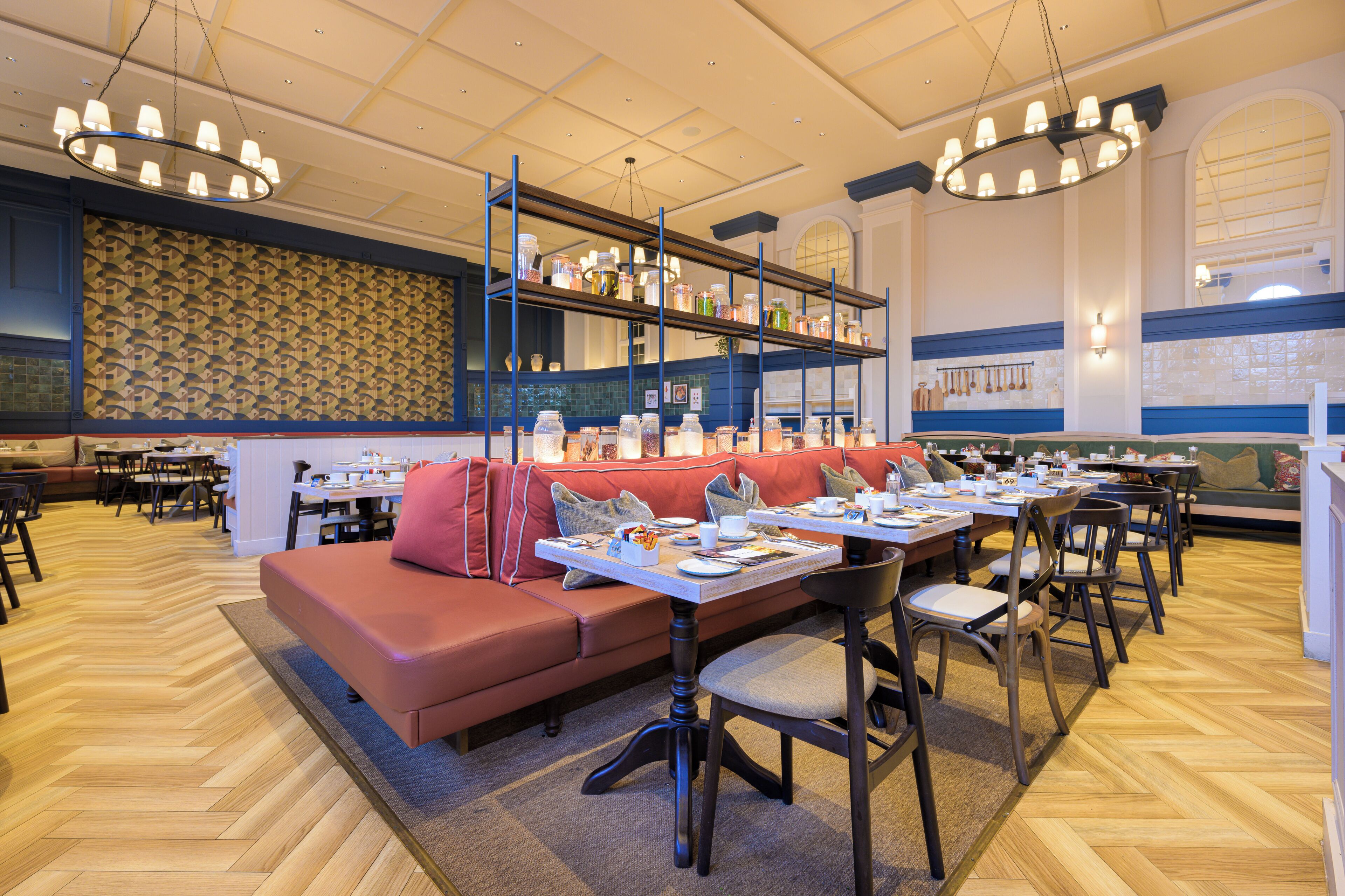 Un restaurant avec un long canapé rouge, de nombreuses tables et des luminaires suspendus.