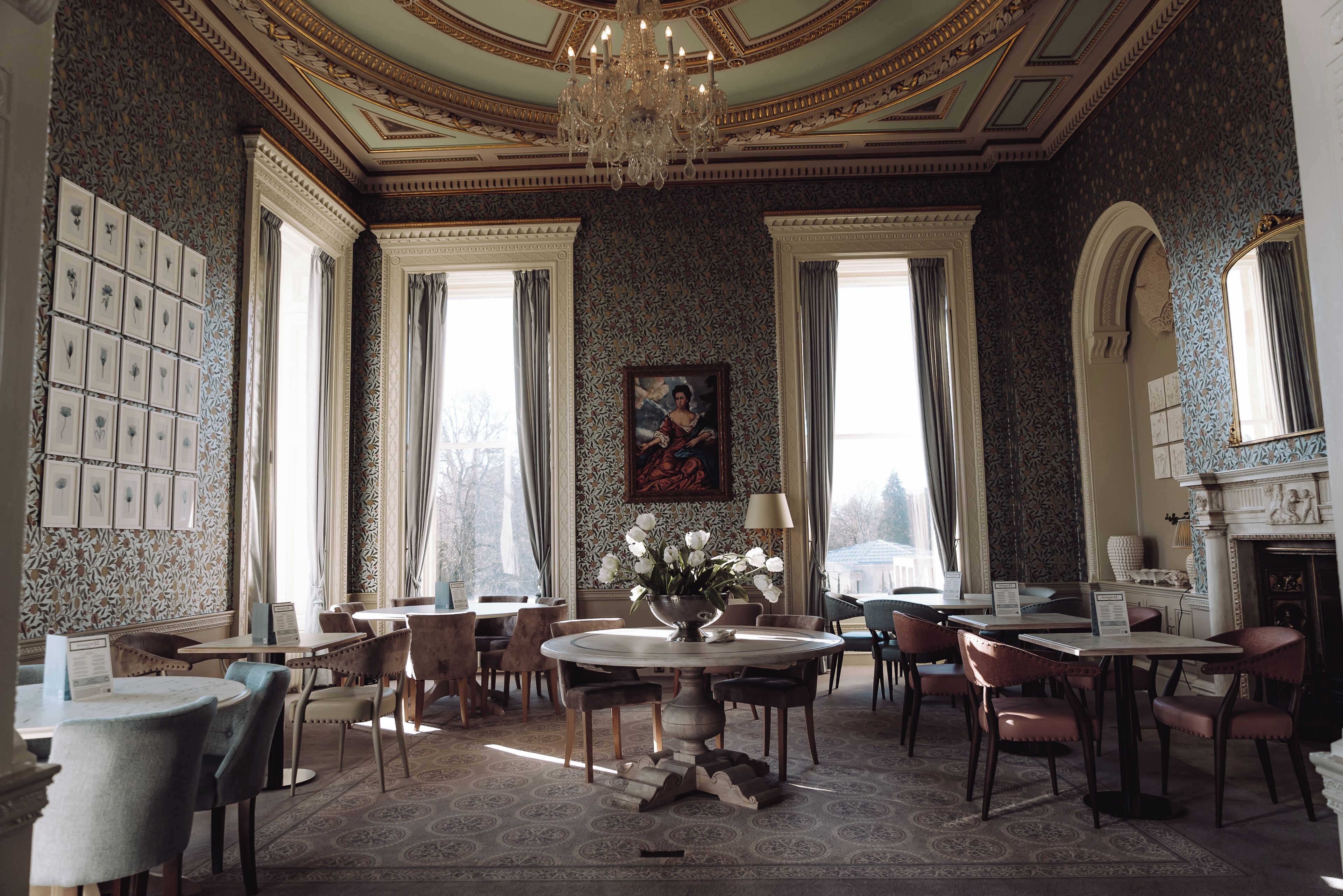 A dining room with a chandelier, patterned wallpaper, and a table with chairs.