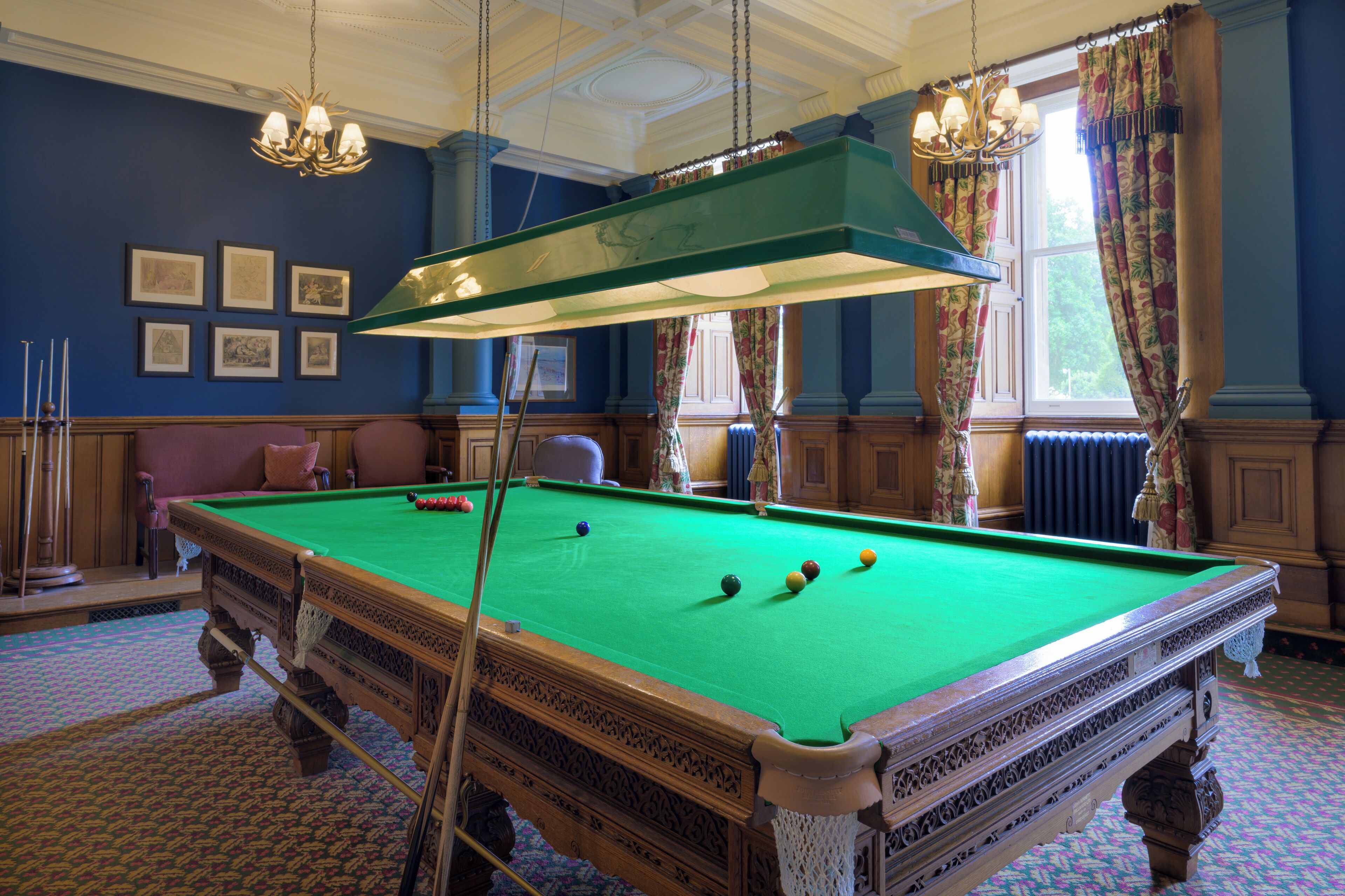 A pool table with balls, a chandelier, and framed pictures on the wall.