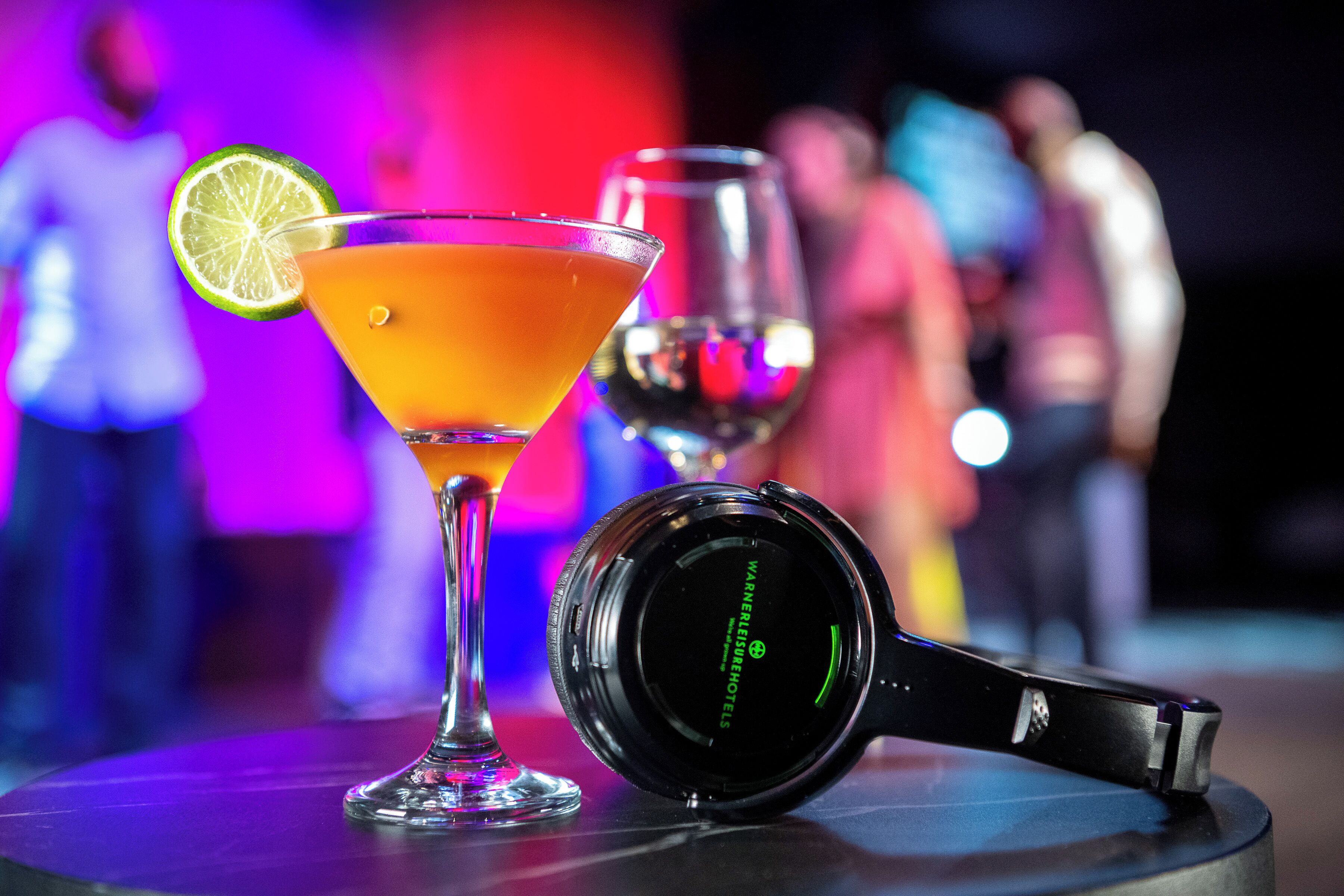 A martini glass with a lime wedge, a wine glass, and a pair of headphones on a table.