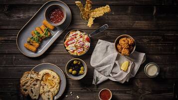 Diversos alimentos como pão, homus, azeitonas e petiscos fritos sobre uma mesa de madeira.