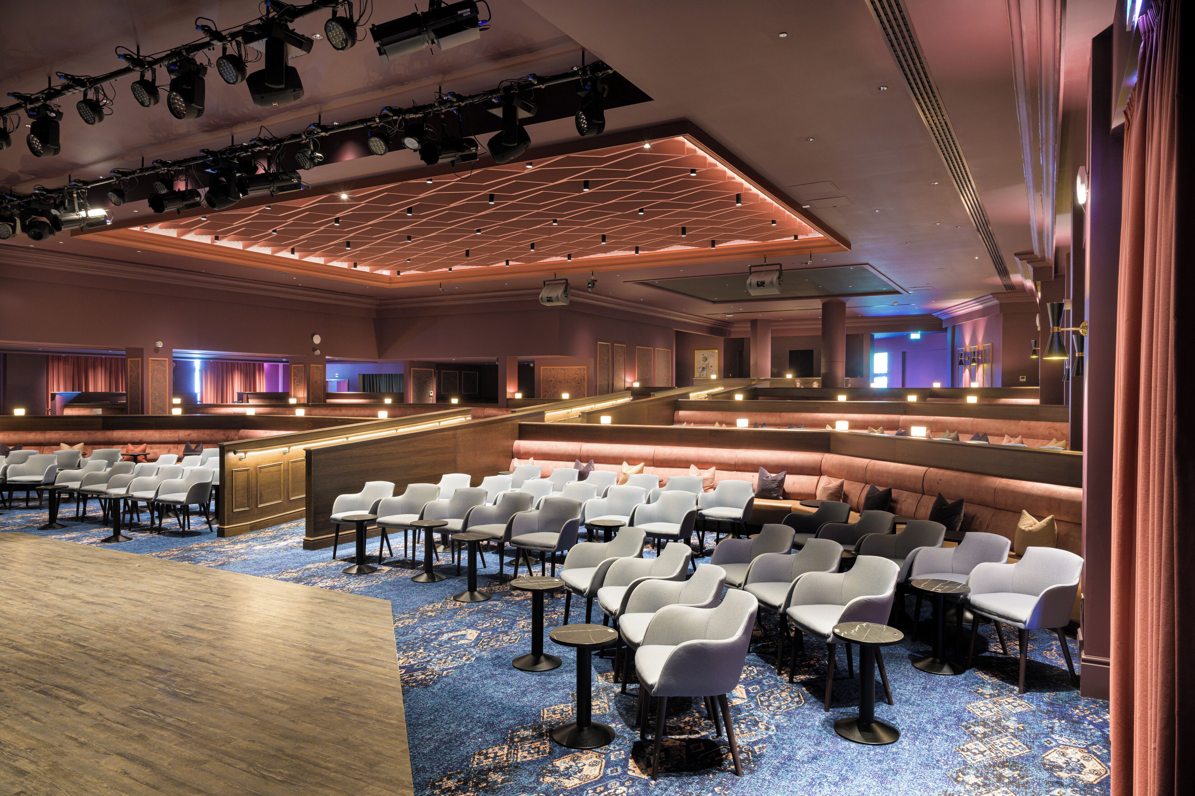 Une salle de conférence spacieuse, avec des rangées de chaises blanches, une scène éclairée et un sol recouvert d’une moquette bleue.