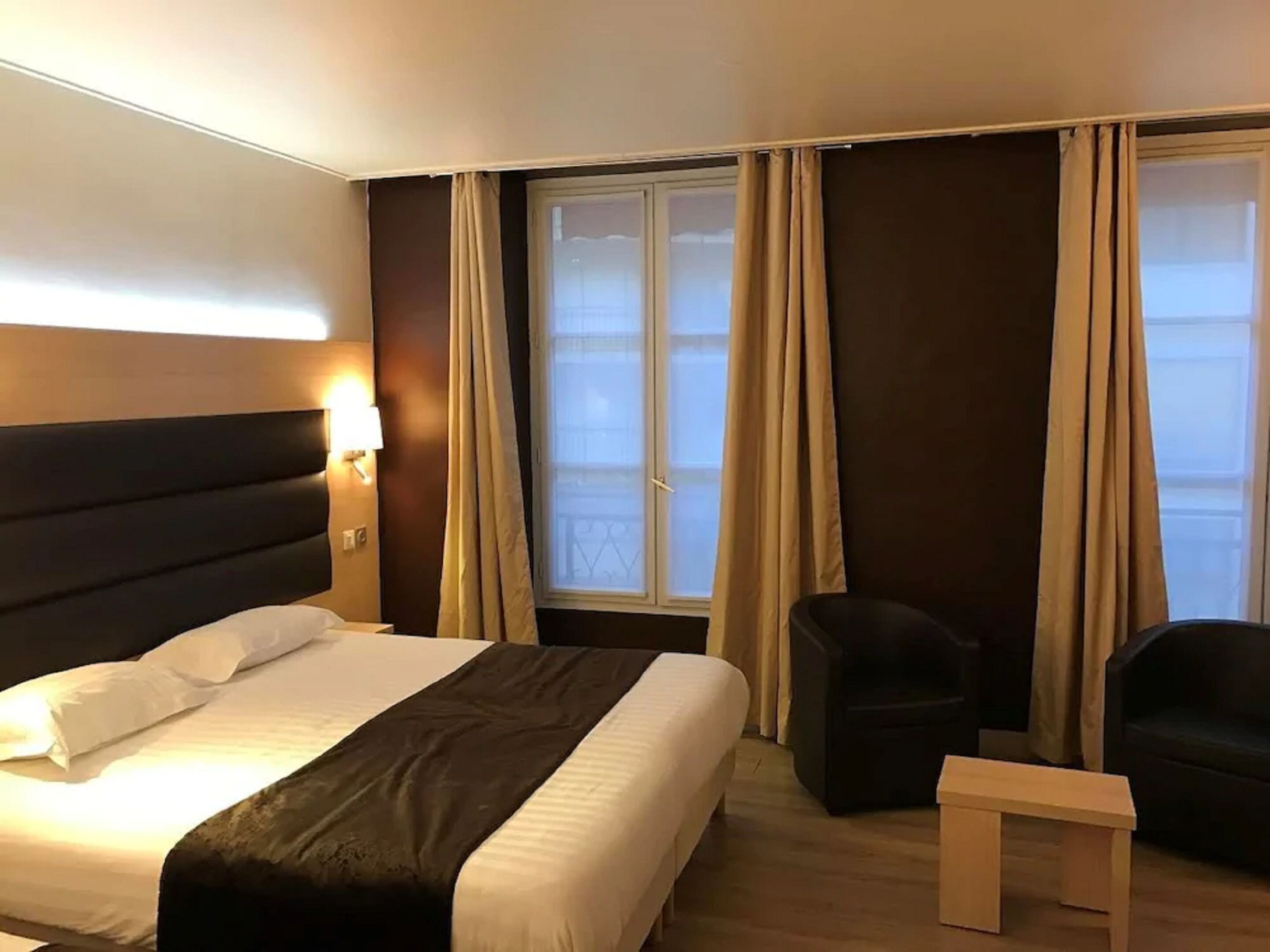 Una camera d'albergo con un letto grande, una sedia, un tavolino e una finestra con tende.