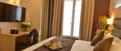 A hotel room with a bed, a desk, a chair, a TV, and a window with curtains.