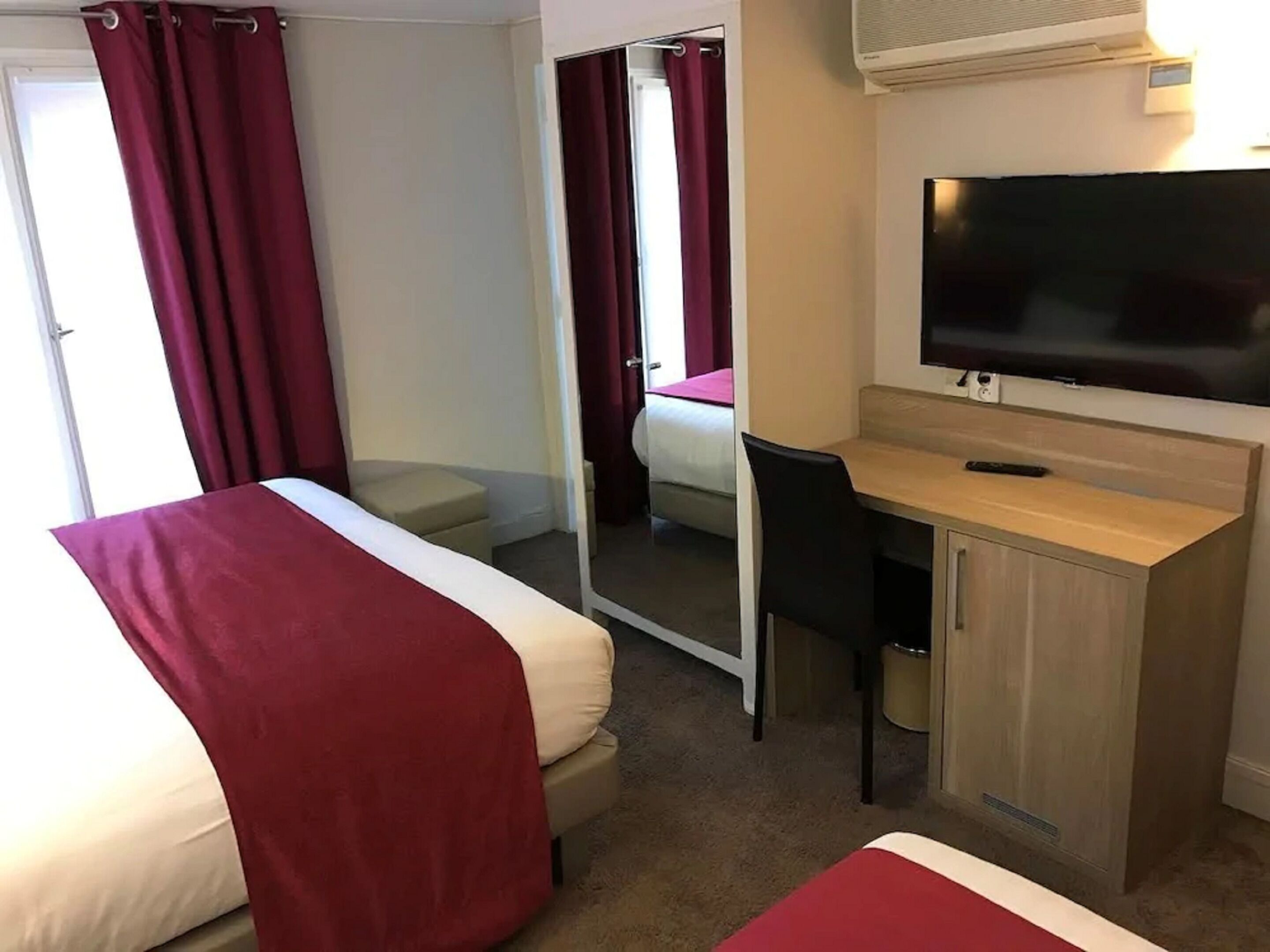 A hotel room with two beds, a desk, a television, and a sliding door.