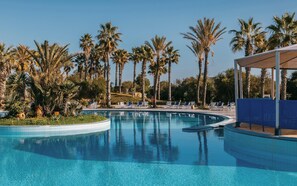 Une piscine à l’eau d’un bleu cristallin, entourée de palmiers et de chaises longues.