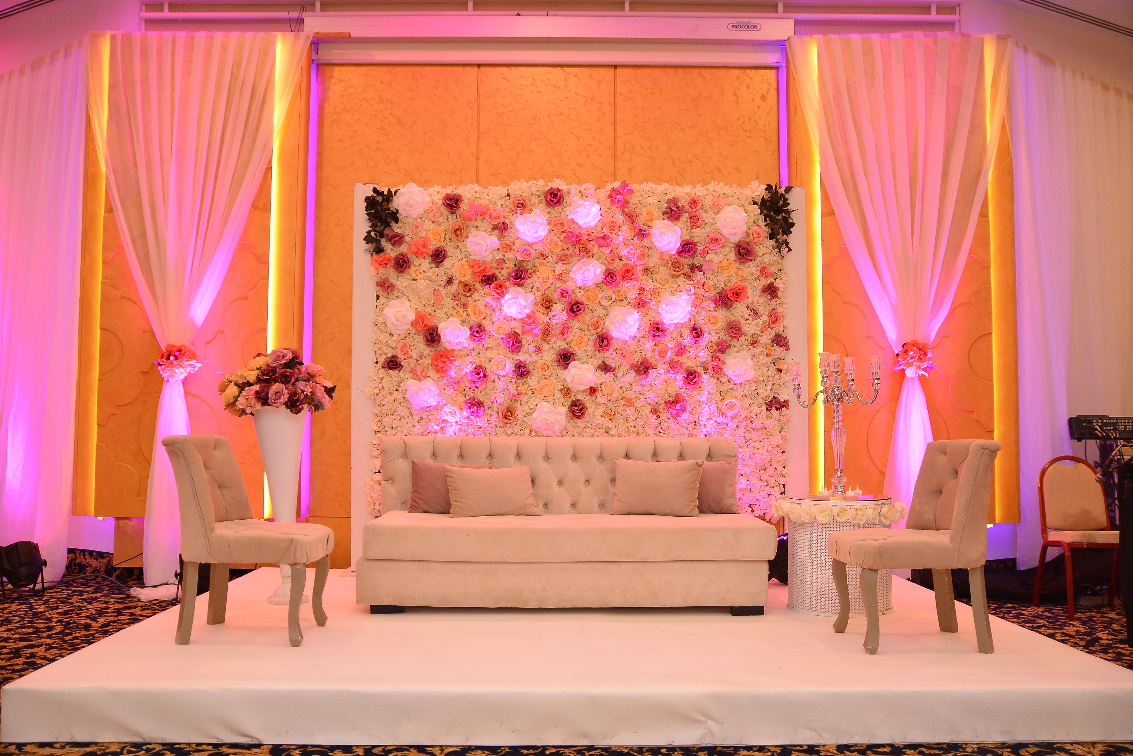 A stage with a floral backdrop, a sofa, and two chairs.