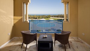 Een balkon met twee rieten stoelen en een kleine tafel, met uitzicht op een zwembad en de zee.