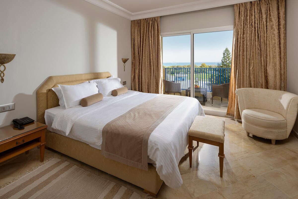 Une chambre d’hôtel avec un grand lit, une chaise, un bureau et un balcon avec vue.