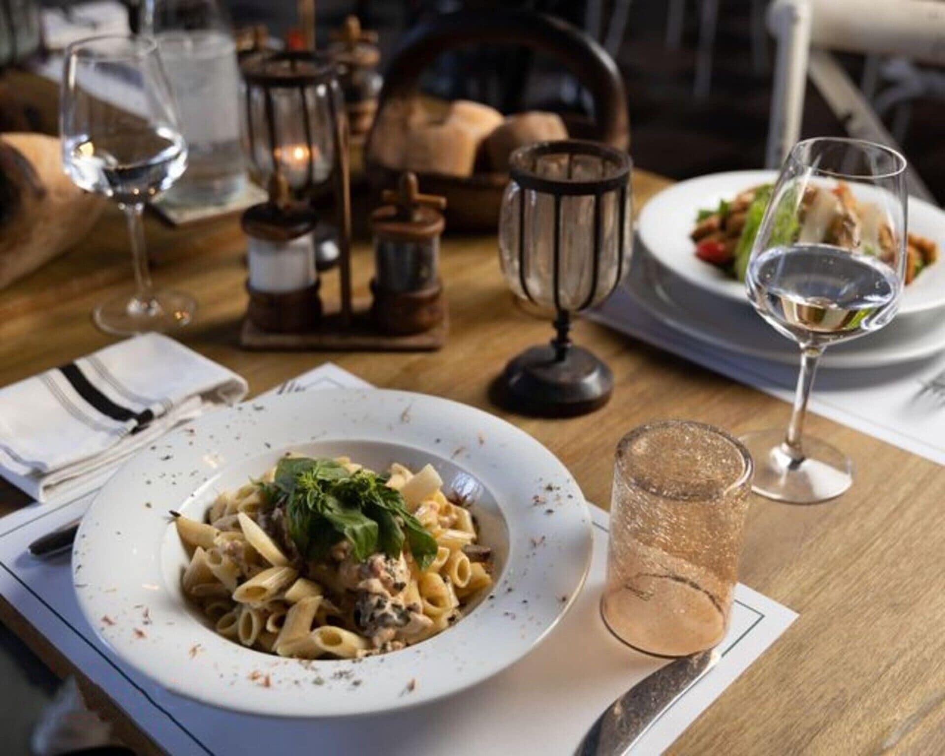 Ein Esstisch mit einer Pasta-Servierplatte, einem Glas Wasser und einer Kerze.