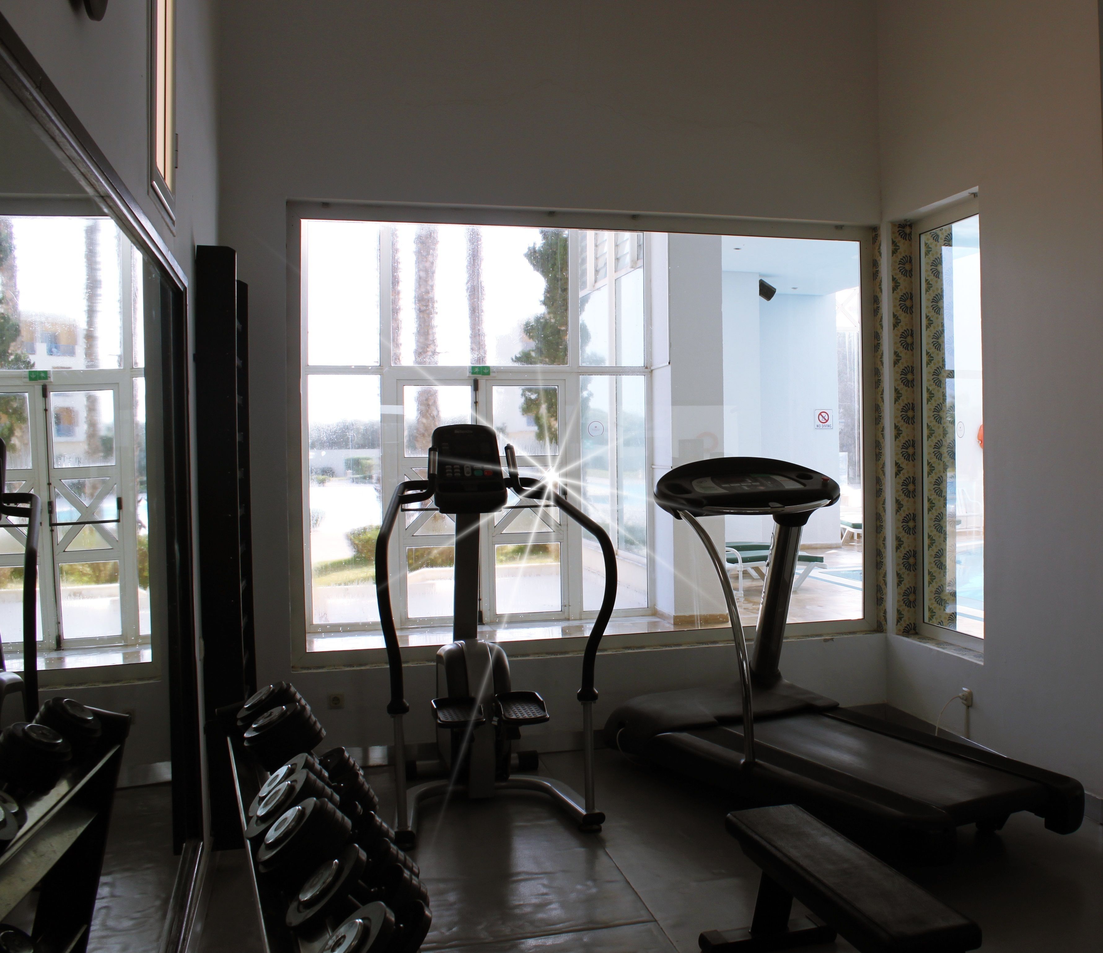 Ein Fitnessstudio mit Laufbändern und Ergometer, große Fenster mit Blick auf die Straße.