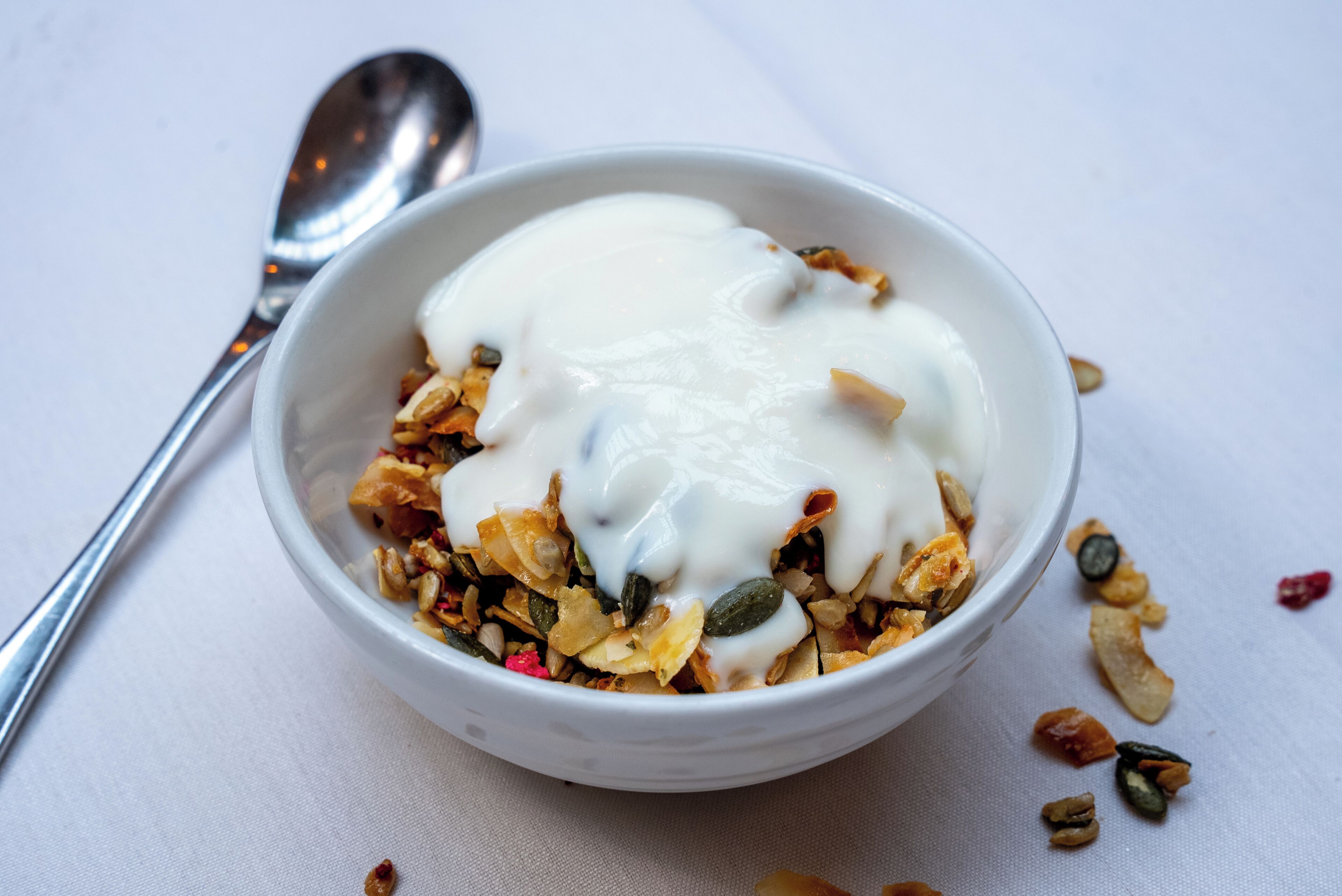A bowl of yogurt with granola and seeds on a white surface.