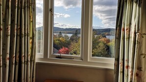A room with a large window offering a view of a lake and autumn foliage. - Lindeth Howe Hotel (Windermere)