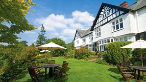 A traditional Tudor-style house with a well-maintained garden, outdoor seating area, and a clear blue sky. - Lindeth Howe Hotel (Windermere)