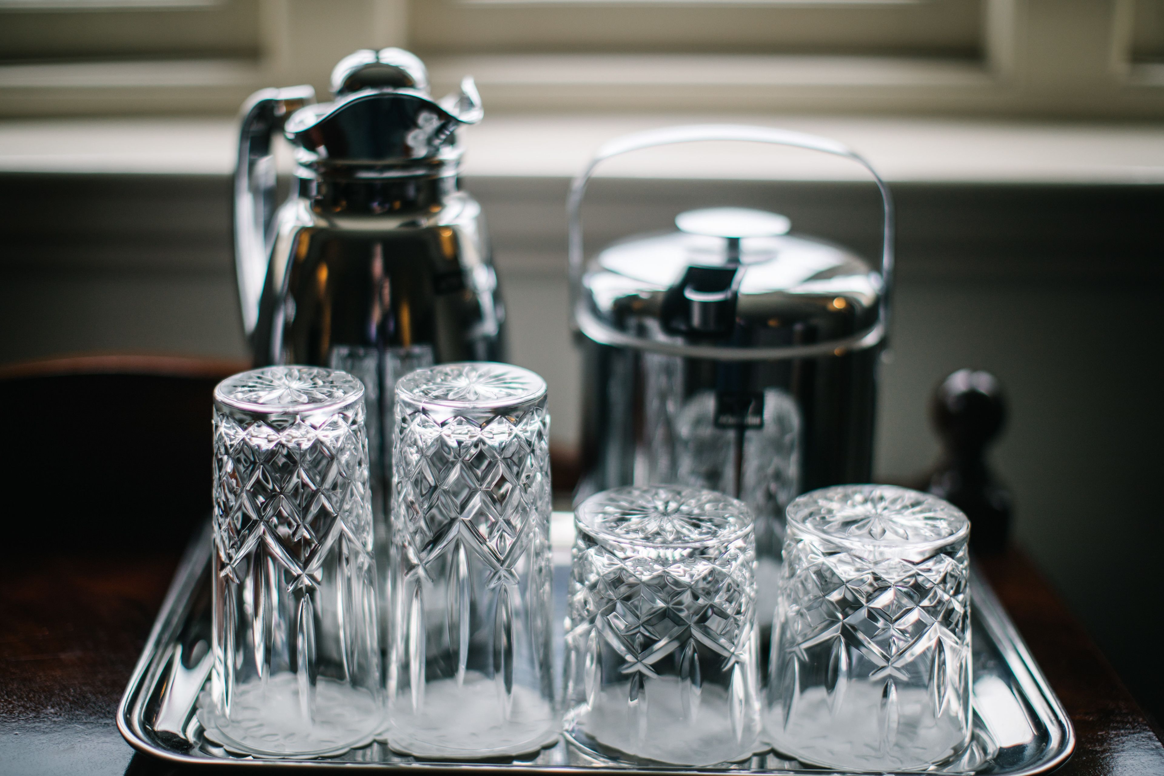 A tray with four crystal glasses and a silver coffee pot on a wooden table.