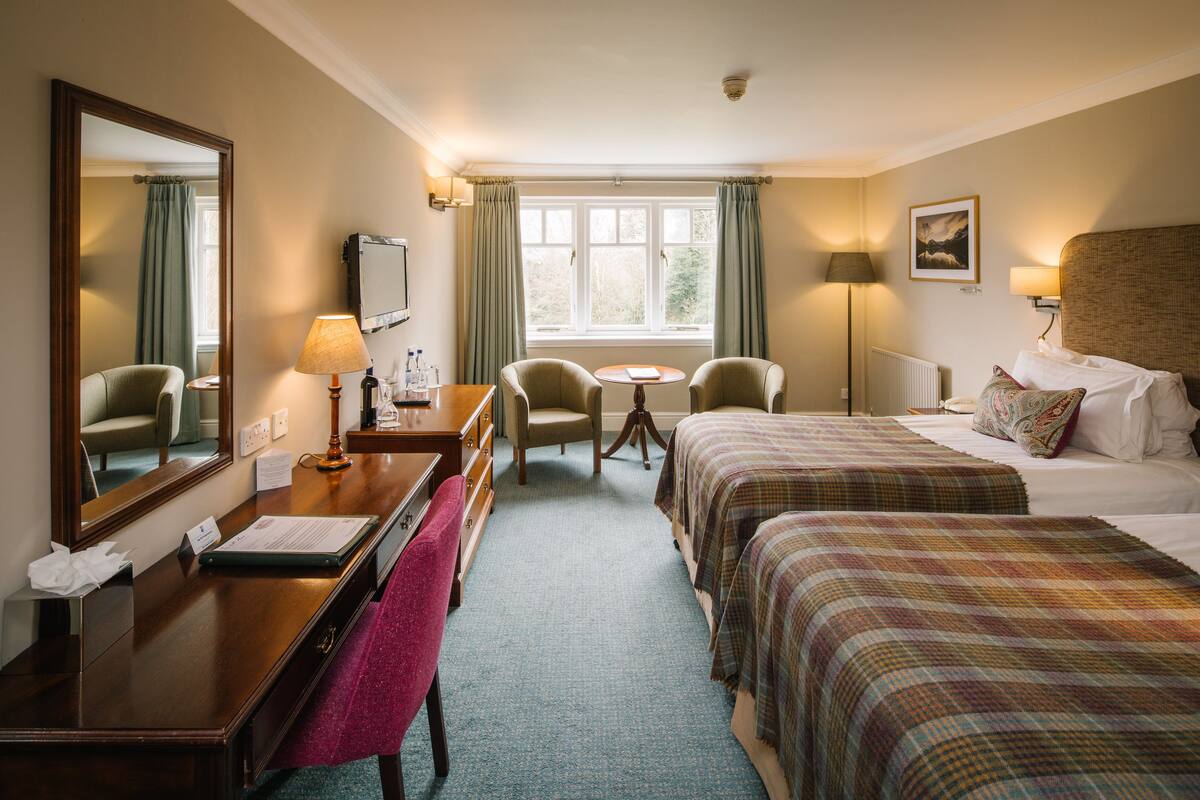 Habitación de hotel con escritorio, dos sillas, cama, ventana y espejo.