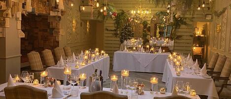 A restaurant with multiple tables set for dining, featuring a high ceiling with natural light and hanging plants.