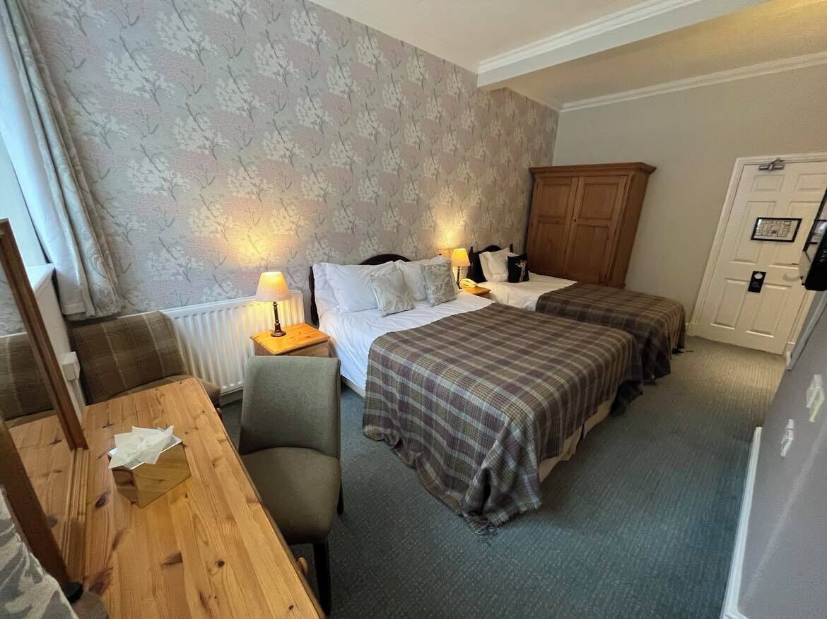 A hotel room with two beds, a wooden table, a chair, a radiator, and a wardrobe.