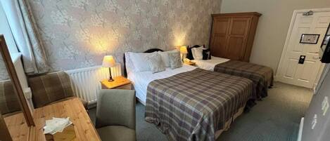 A hotel room with two beds, a wooden table, a chair, a radiator, and a wardrobe.