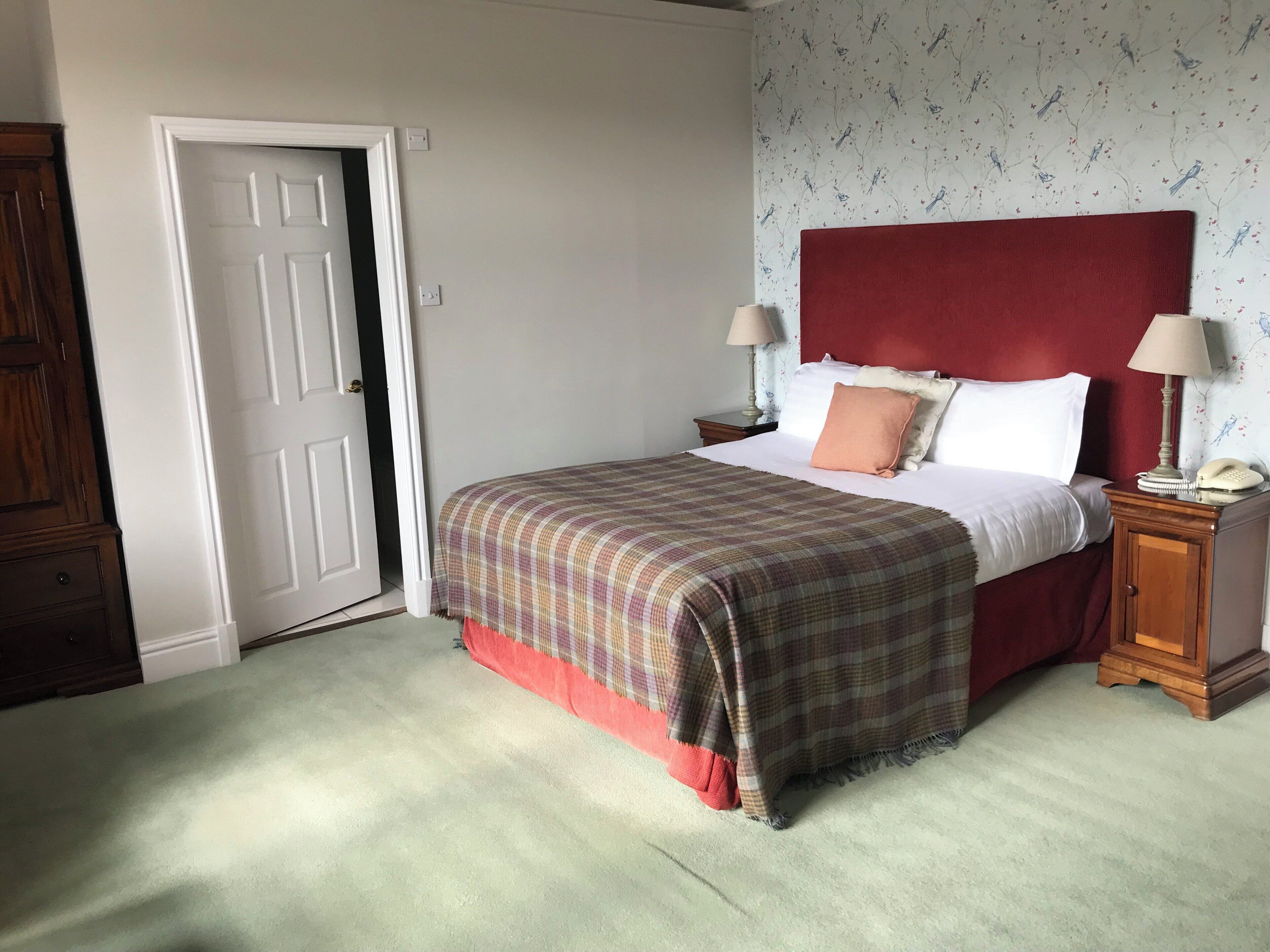 Quarto com cama, duas mesas de cabeceira, uma porta e uma parede com padrão floral.