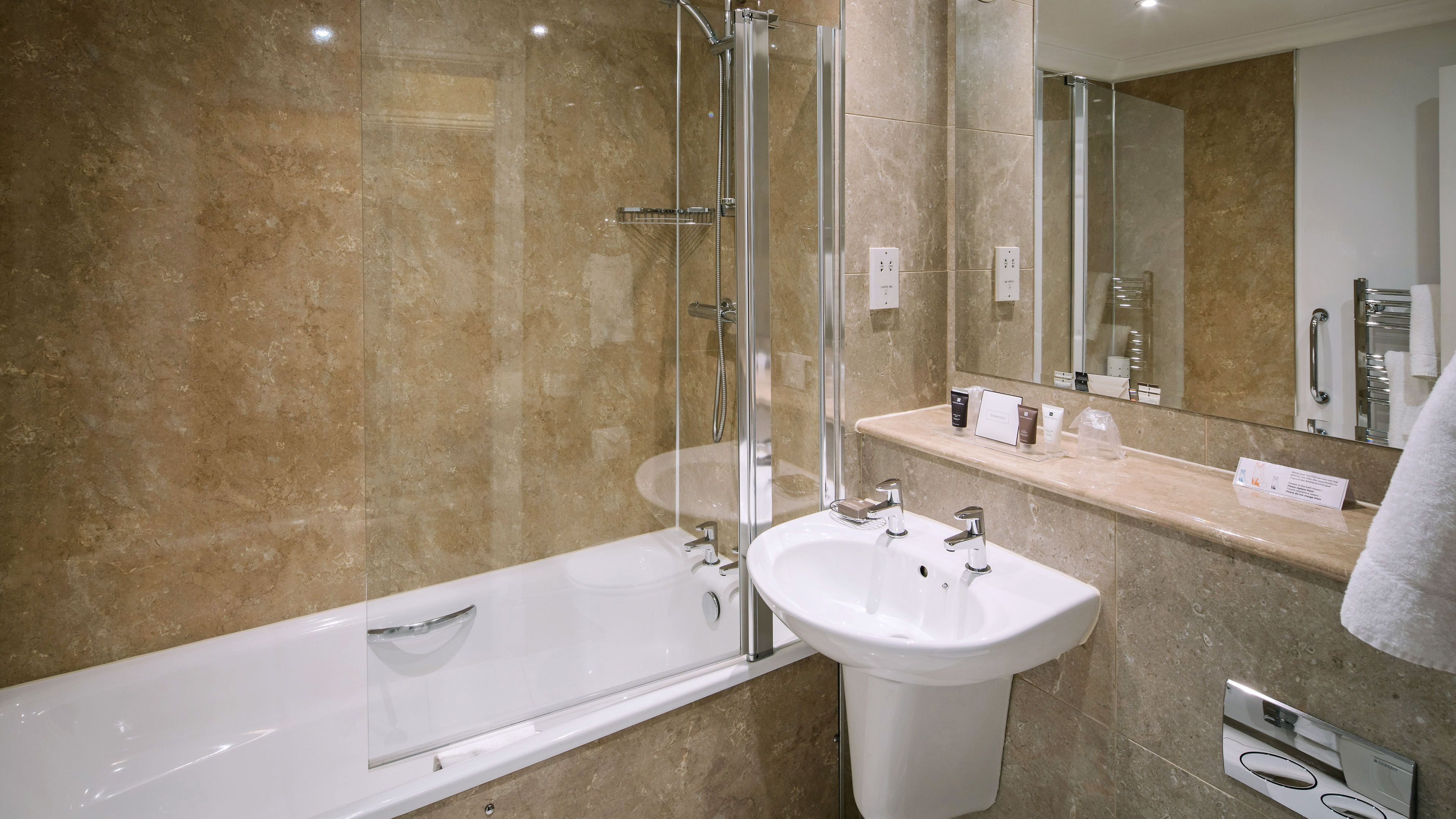 Un bany modern amb dutxa de vidre, un lavabo blanc i un mirall gran.