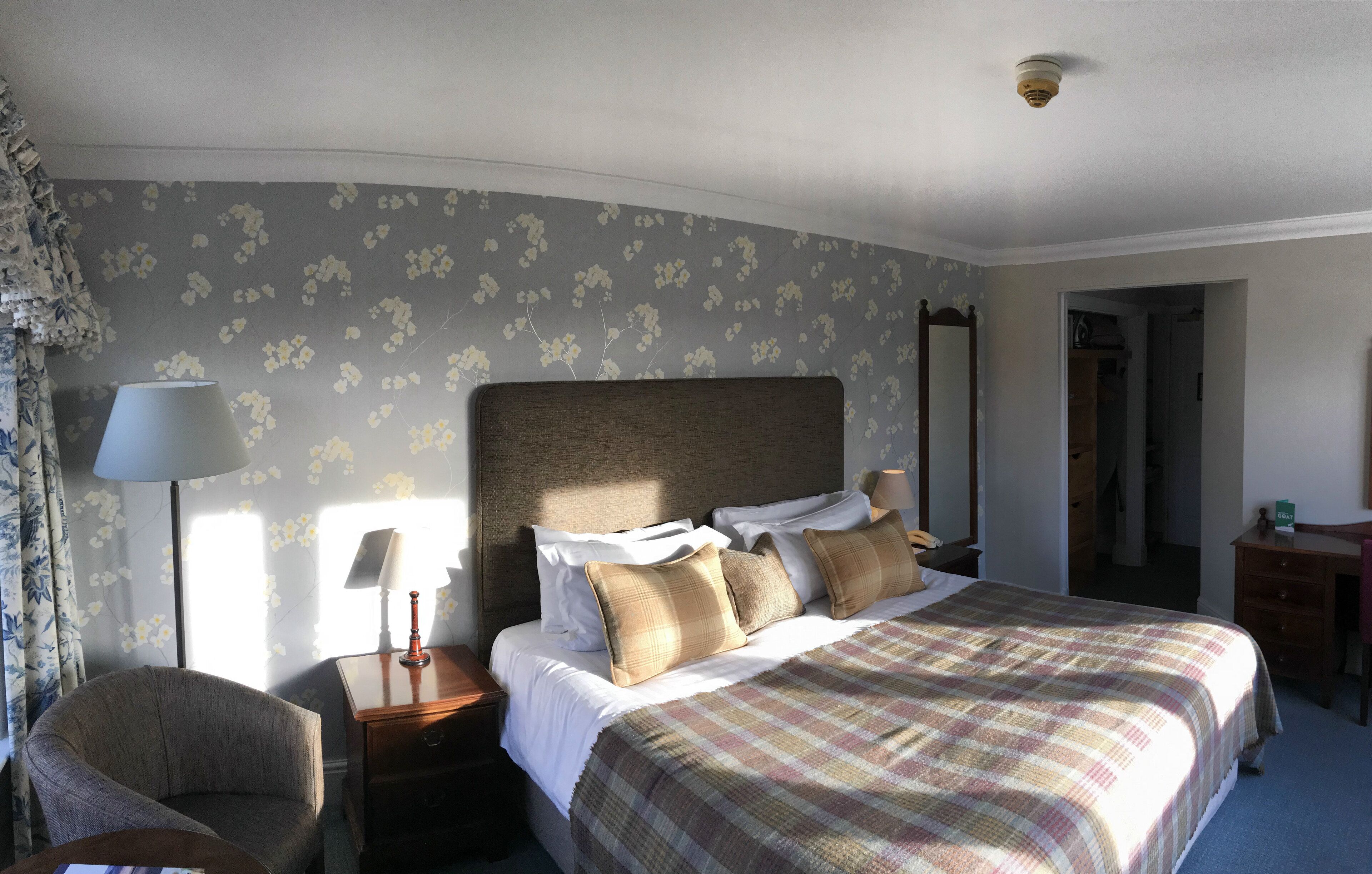 A hotel room with a large bed, a chair, a nightstand, a lamp, and a wardrobe.