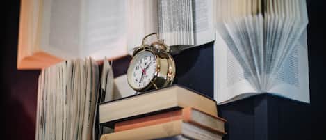 A stack of books with an alarm clock on top, surrounded by more books.