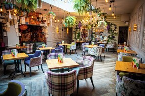 A cozy restaurant with wooden tables and plaid chairs, surrounded by hanging plants and bookshelves. - Lindeth Howe Hotel (Windermere)