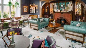 A cozy living room with a fireplace, comfortable seating, and a view of the outdoors. - Lindeth Howe Hotel (Windermere)