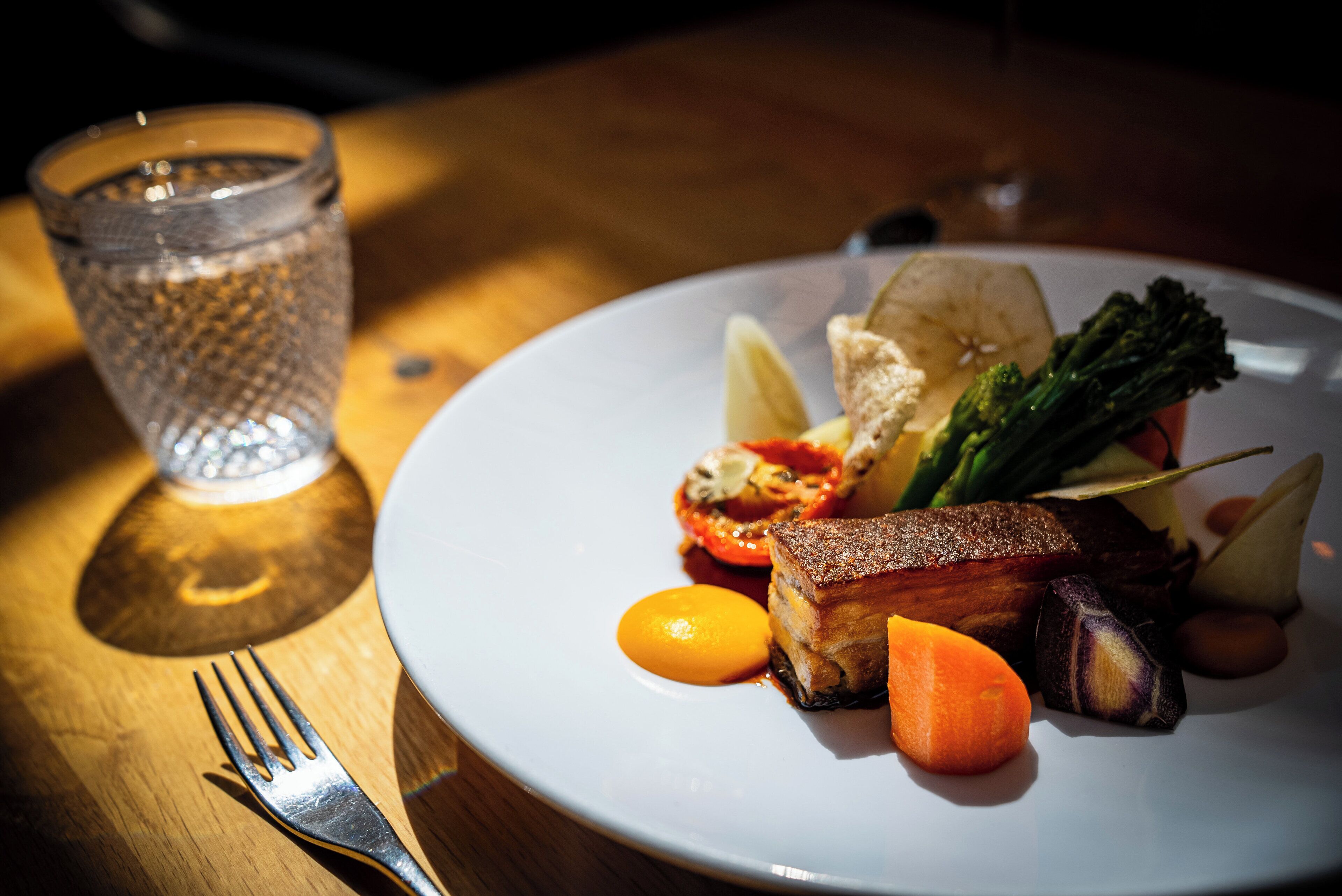 A plate of food with a fork and a glass of water on a wooden table.