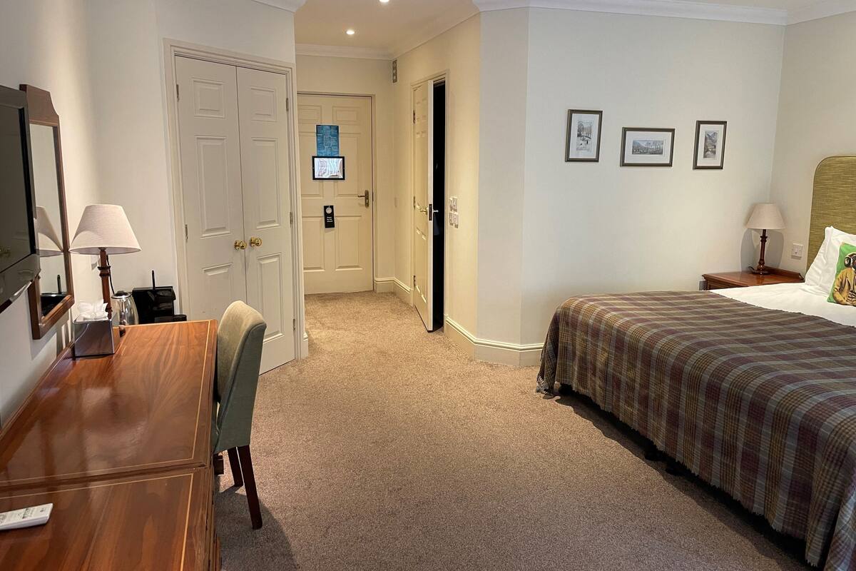 Habitación de hotel con cama, escritorio con lámpara, silla y televisión en una esquina.