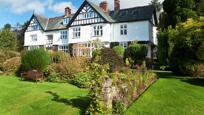 A large, white, Tudor-style house with multiple chimneys, surrounded by well-maintained gardens and a bench. - Lindeth Howe Hotel (Windermere)