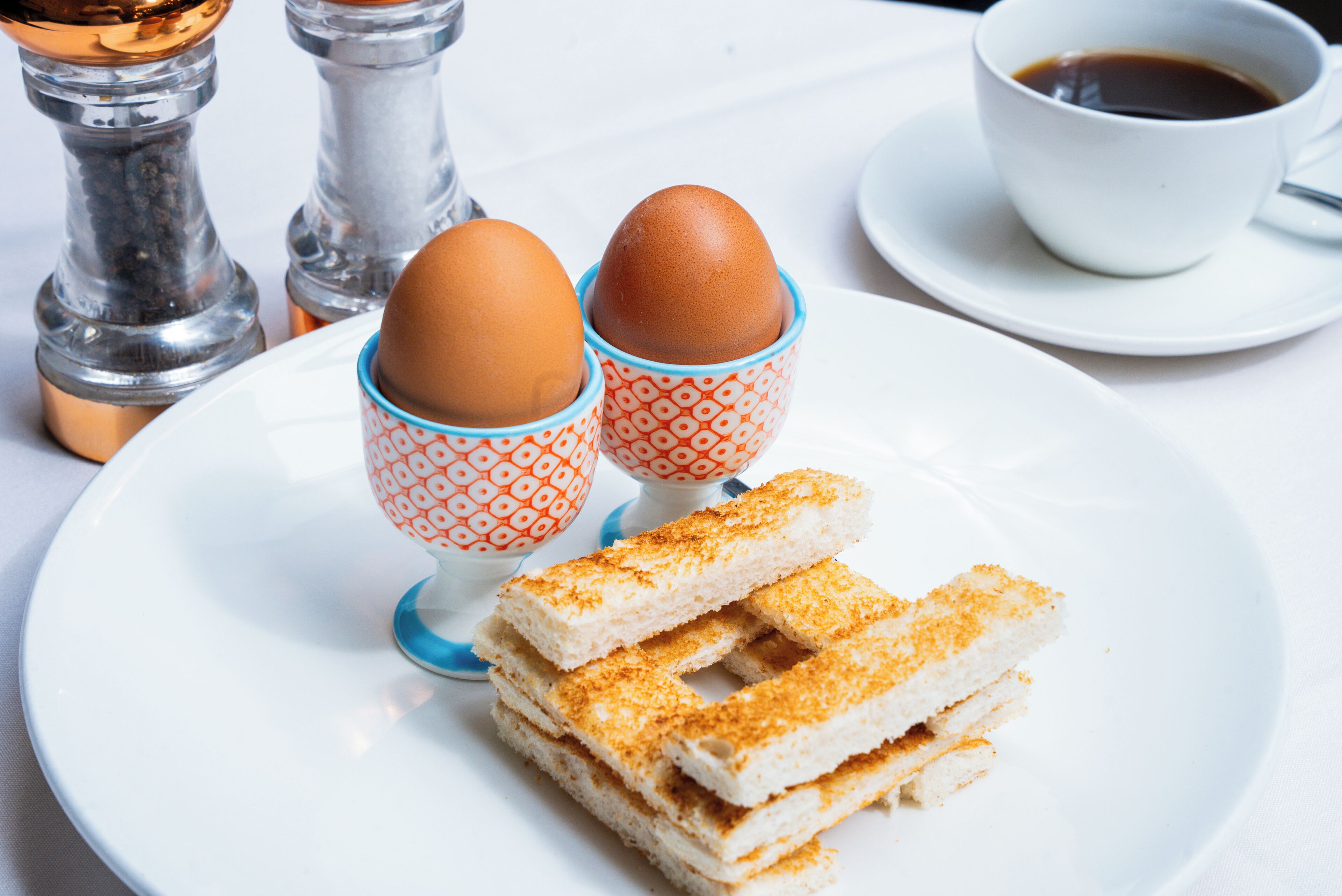 Un plato con dos huevos en recipientes estampados, una taza de café y una pila de pan.