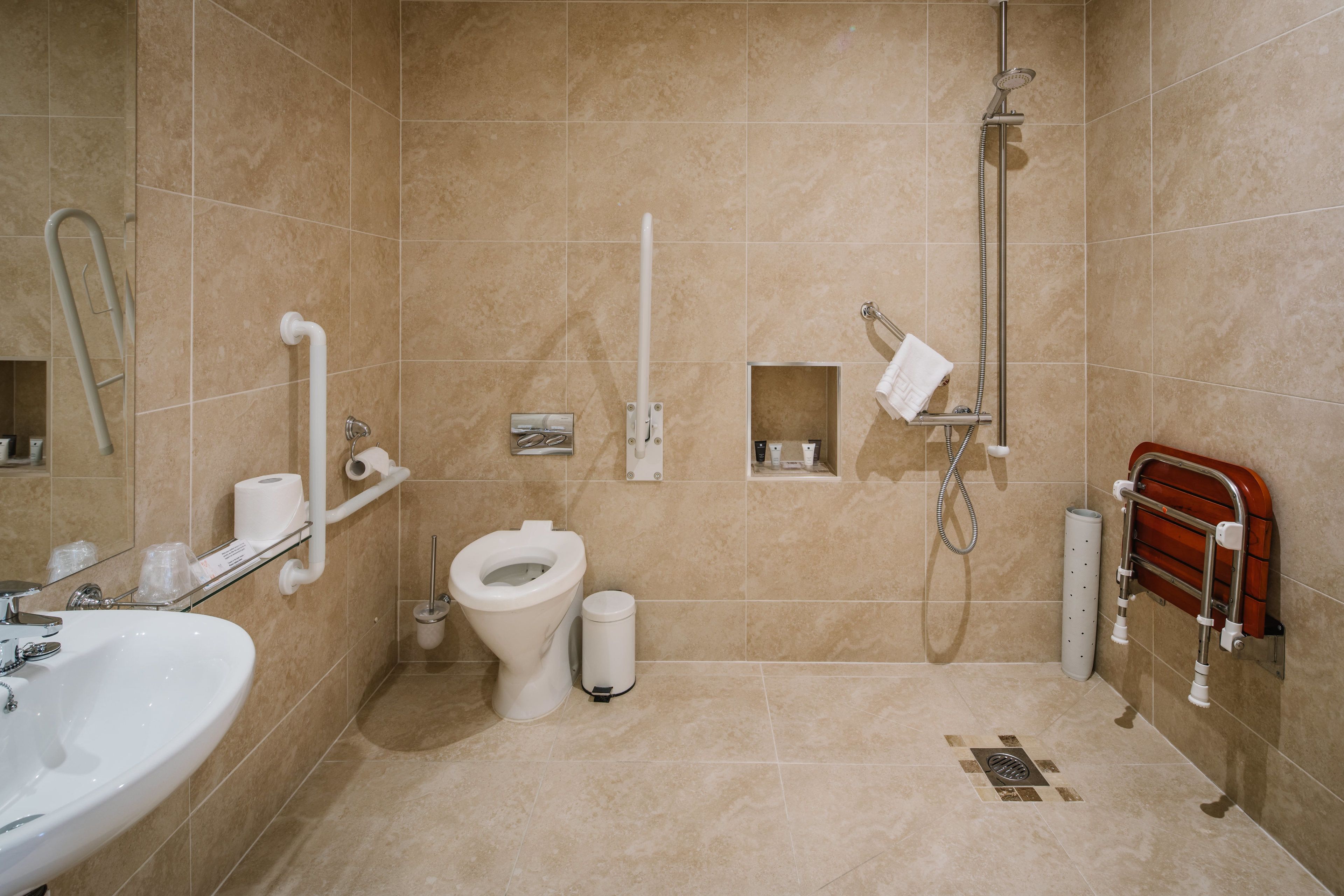 A bathroom with a toilet, bidet, shower, and a handrail.