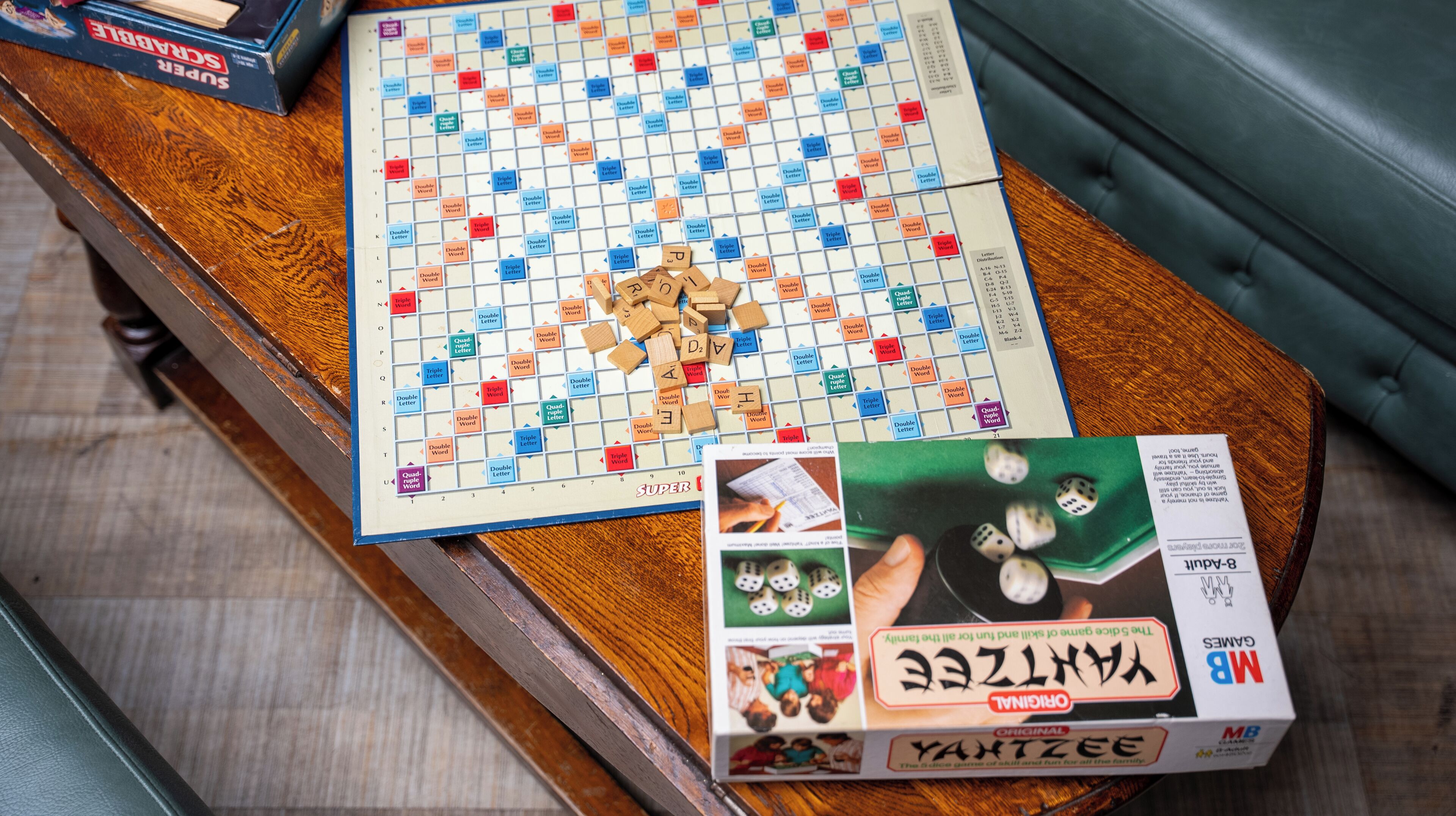 A Scrabble board game on a wooden table with dice and a box of Yatzee dice.