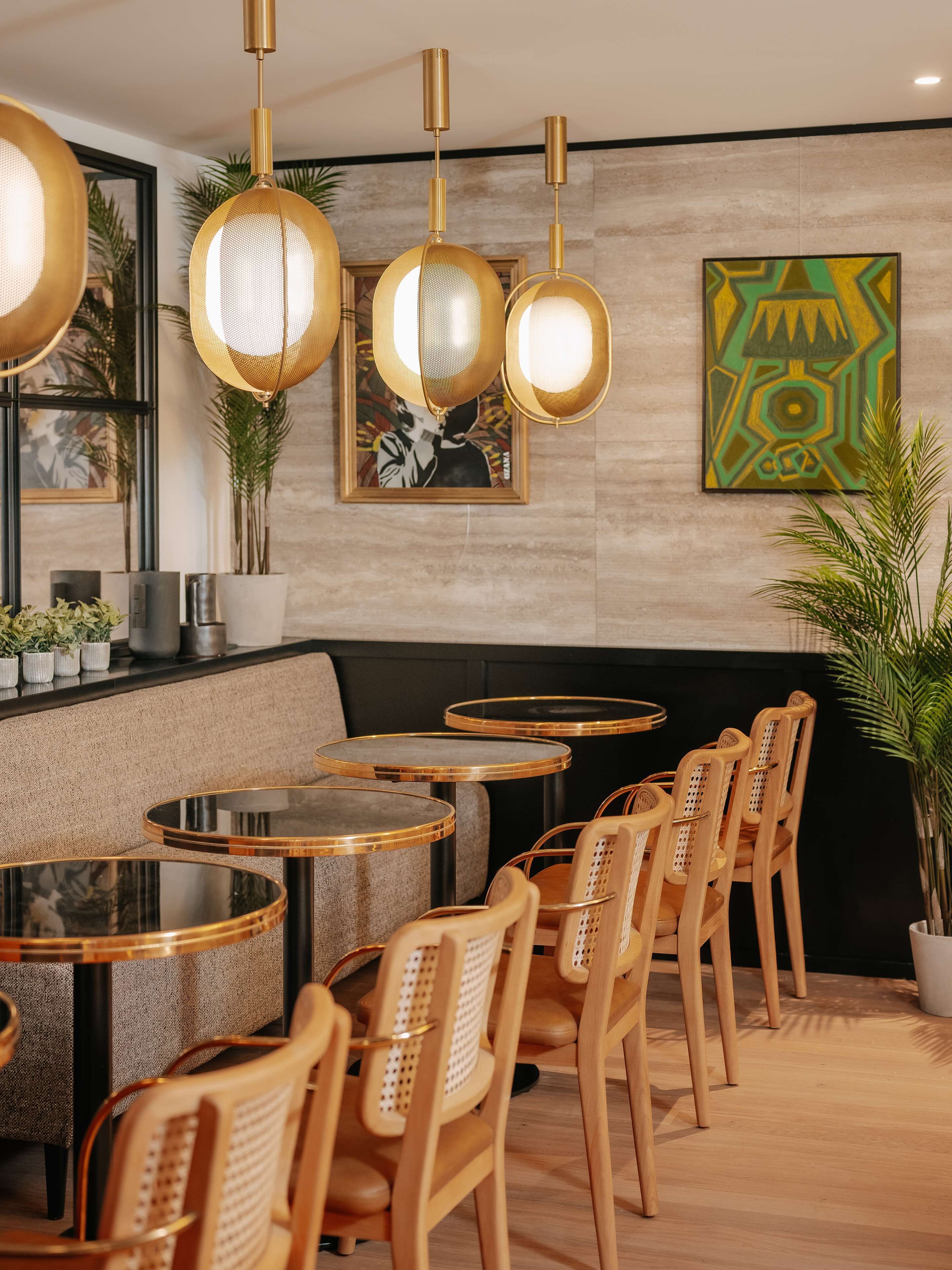 A modern restaurant interior with round tables, wooden chairs, and hanging gold pendant lights.
