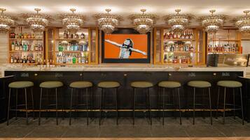 Een bar met meerdere krukken, een groot kunstwerk in een lijst en gevulde flessen op planken.