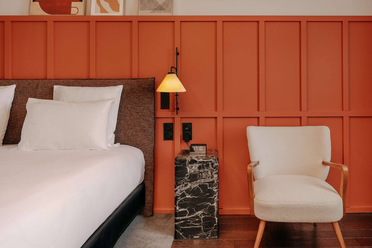 A hotel room with a bed, a nightstand, a lamp, and a chair.