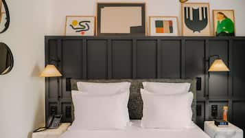 Una habitación de hotel con una cama grande, dos lámparas de noche, un teléfono en la pared y un reloj digital que marca las 09:53.