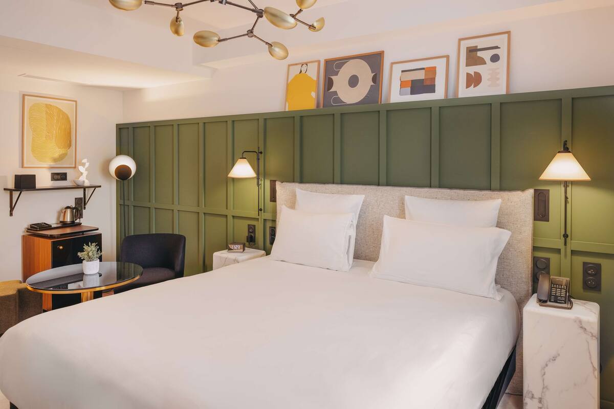 A neatly arranged hotel room with a large bed, bedside lamps, a small table with a lamp, and artwork on the wall.