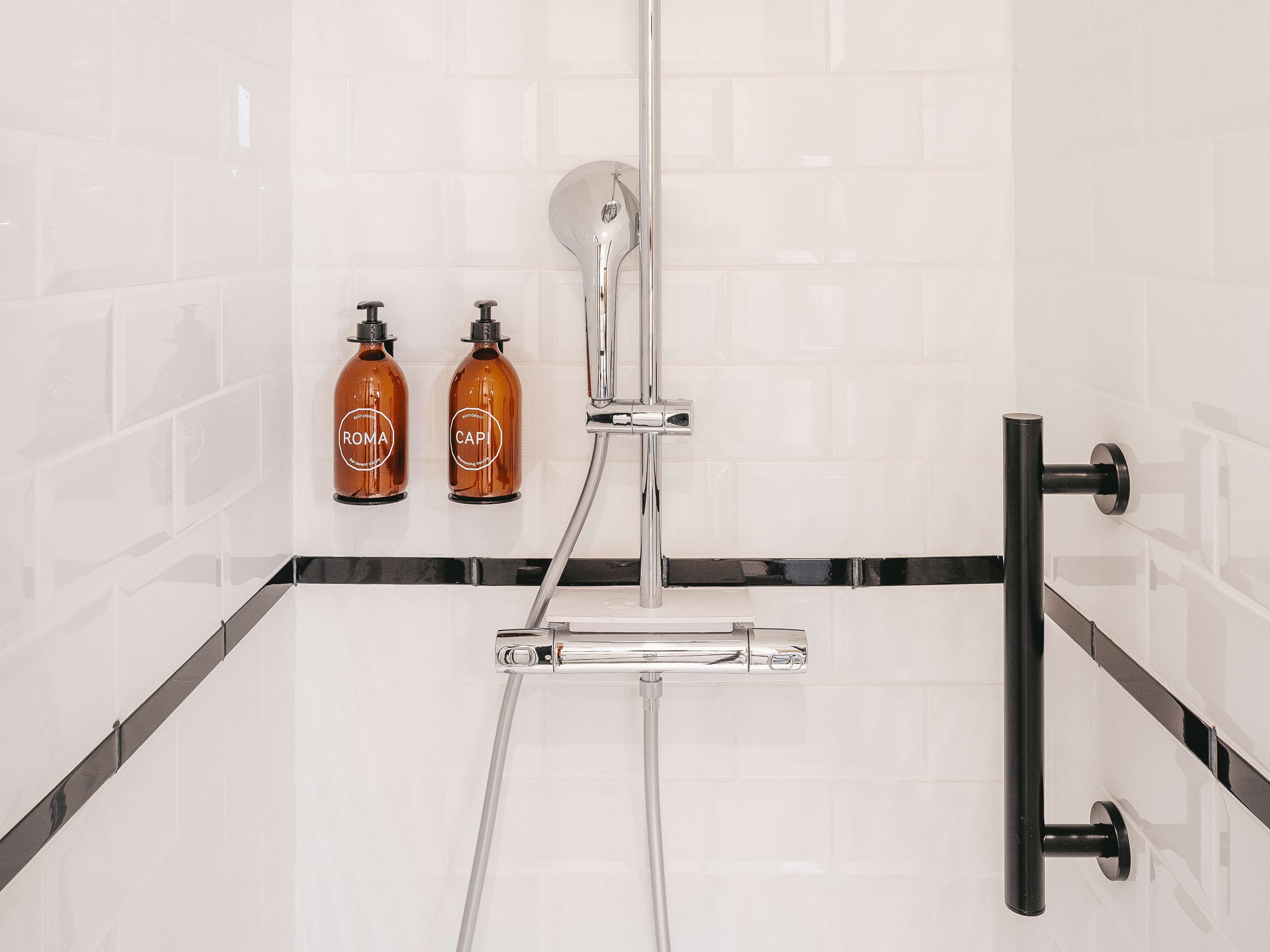 A modern bathroom with a glass shower enclosure, two bottles of shampoo, and a black towel rack.